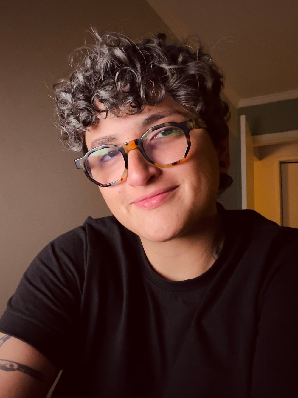 Portrait of Lorenza Quinzi: smiling, with curly hair and tortoiseshell glasses, in a black t-shirt.